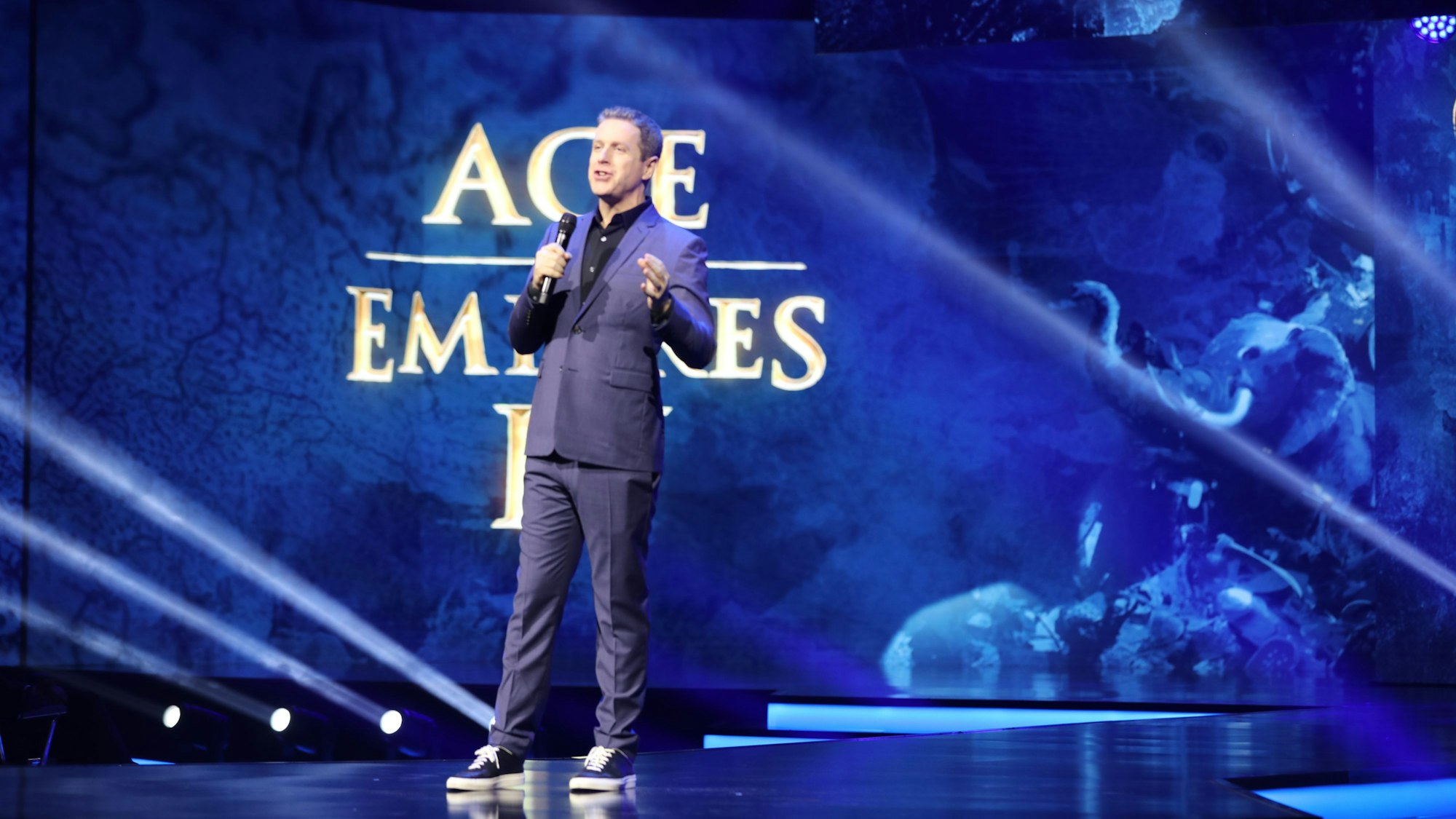 Moderator Geoff Keighley steht bei der Gamescom Opening Night Live 2023 auf der Bühne, im Hintergrund wird das Spiel ‚Age of Empires IV‘ vorgestellt.