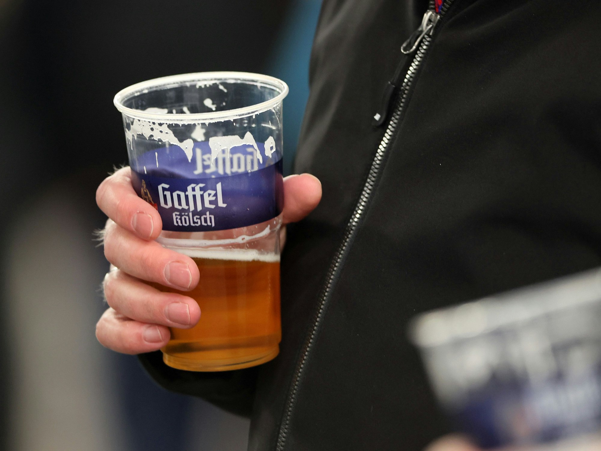 Ein Fan von Fortuna Köln hält einen Bier-Becher in der Hand.