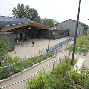 Ein modernes Schulgebäude,davor fahren drei Kinder Fahrrad.