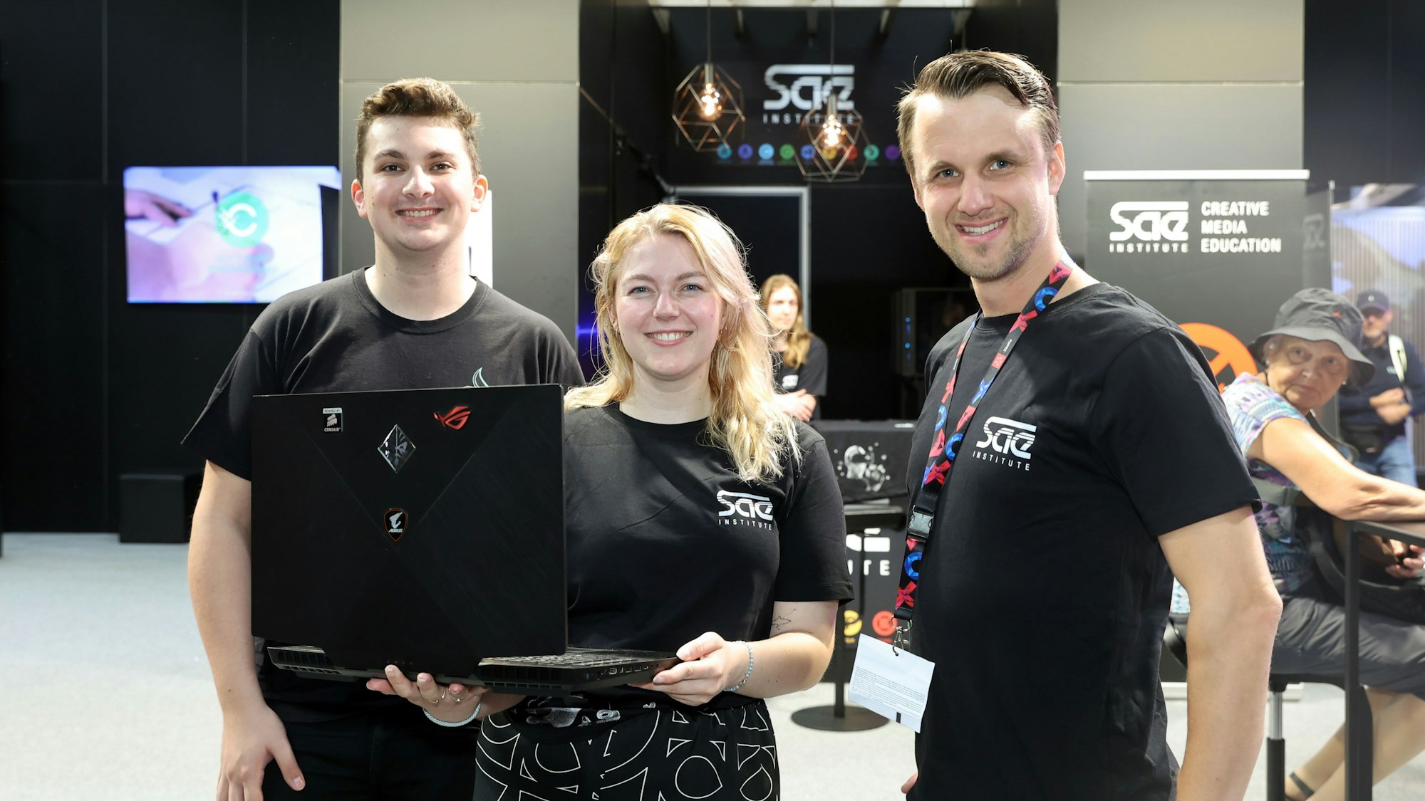 Drei Menschen stehen an einem Stand auf der Gamescom in Köln.