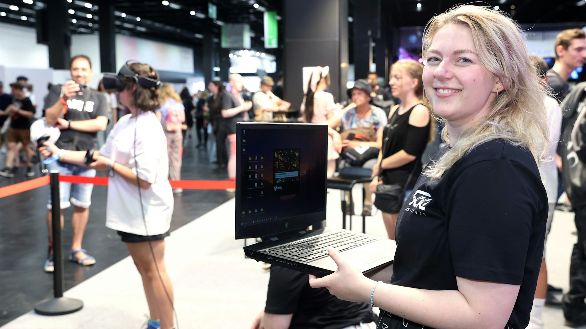 Kira Hajmann steht auf der Gamescom und hält einen Laptop in der Hand.