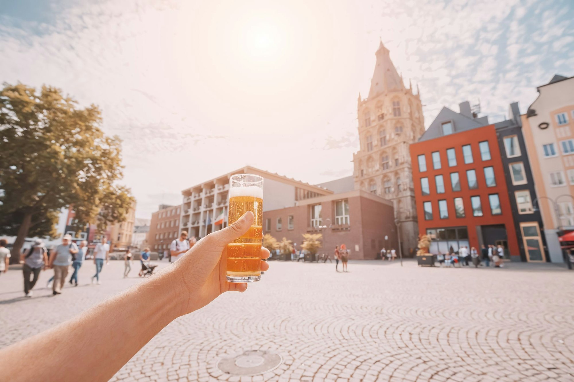 Hand with traditional Cologne koelsch beer in outdoor pub with old town square in background