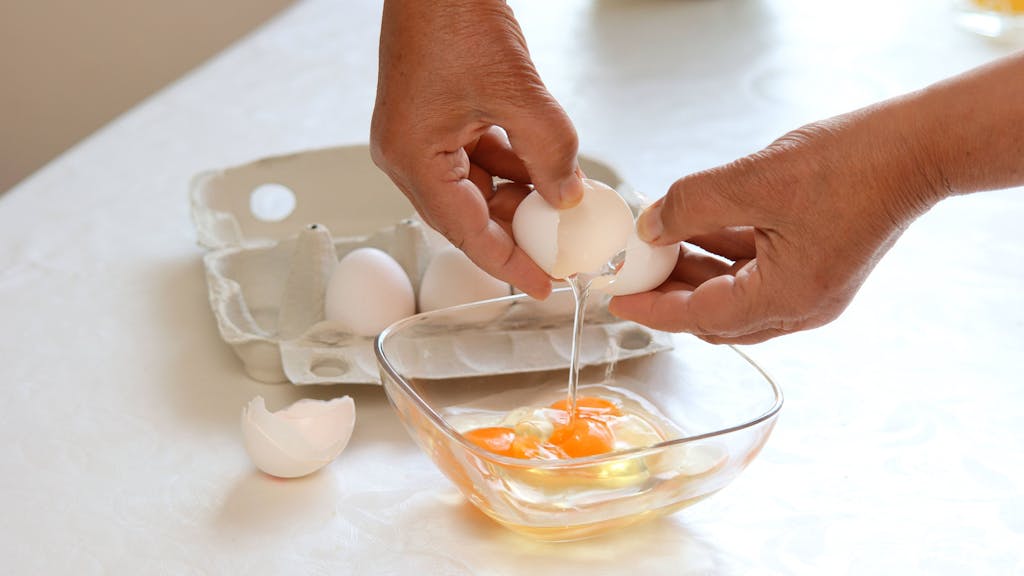 Eine Frau schlägt Eier in eine Schüssel auf.