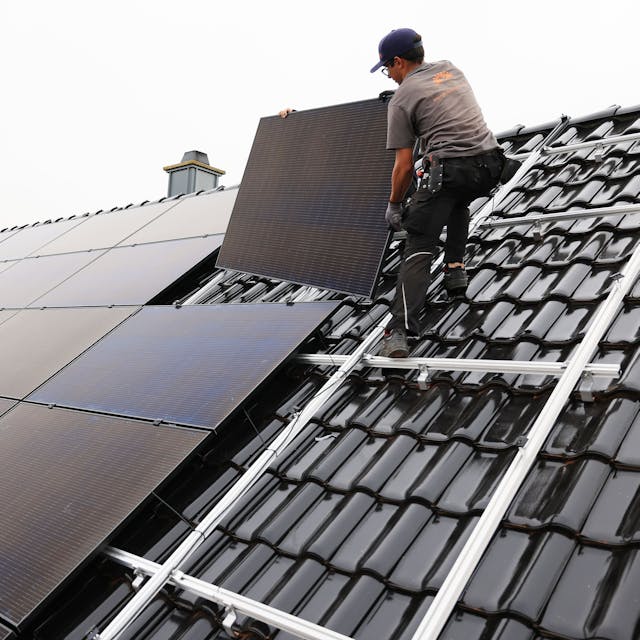 Handwerker montieren Solarmodule auf dem Dach eines Wohnhauses.