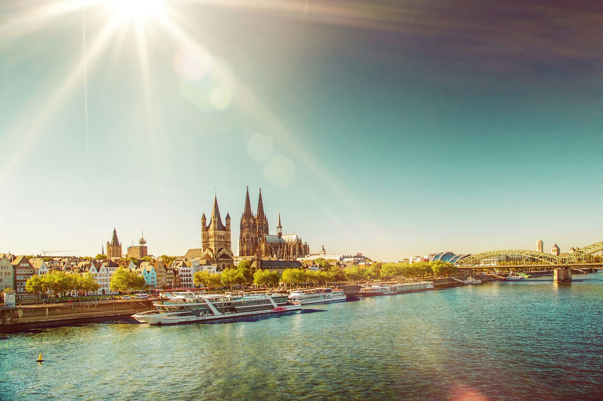 View on the old town of Cologne and Cologne Cathedral with Hohenzollern Bridge and several white passenger boats on the river Rhine on a sunny day in summer