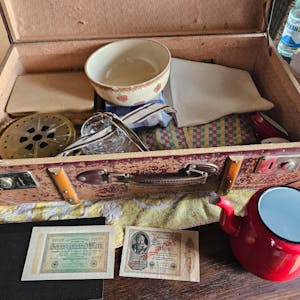 Ein Koffer mit Tüchern, einer Kaffeekanne und alten Geldscheinen ist zu sehen.