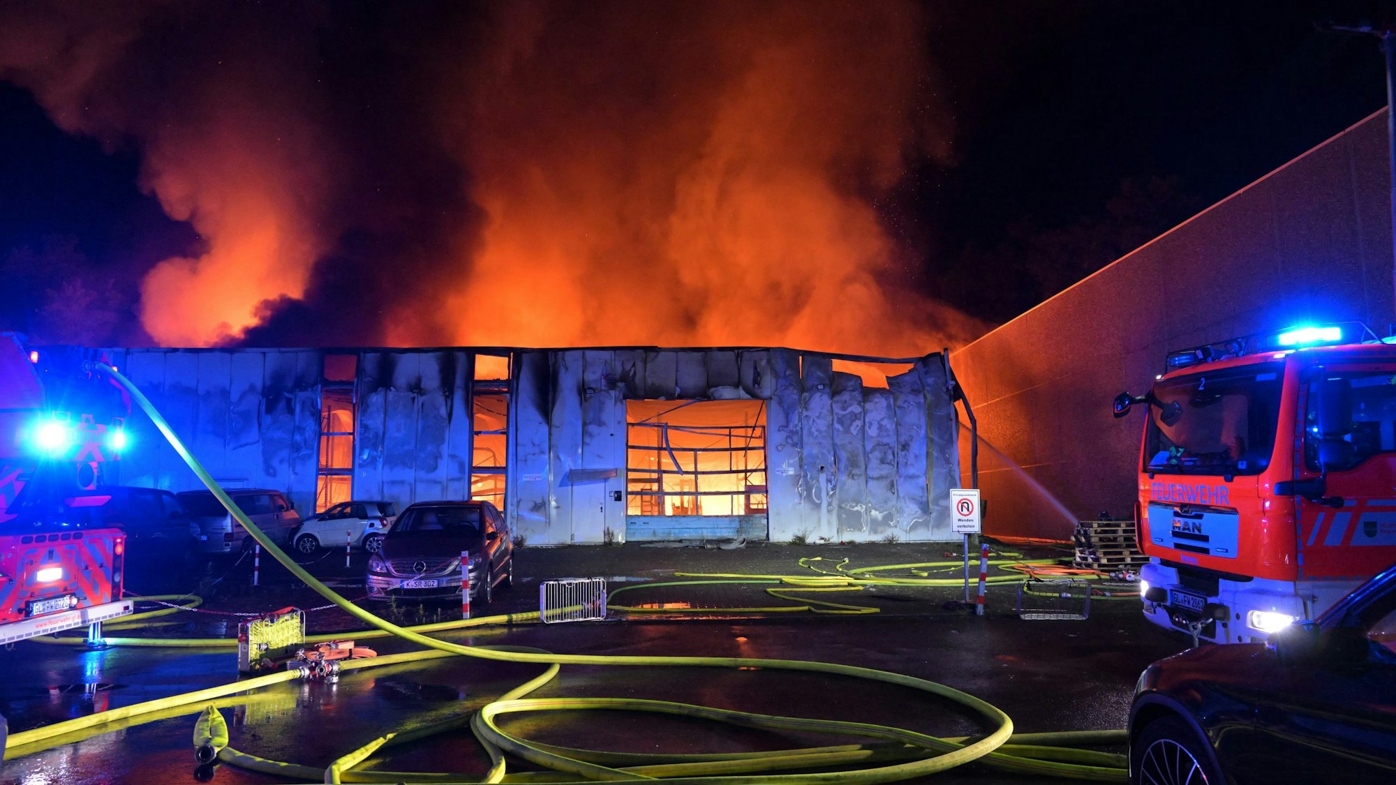 Flammen schlagen aus einer Industriehalle im Gewerbegebiet „Auf der Kaule“ in Refrath, Feuerwehrleute versuchen den Brand zu löschen.
