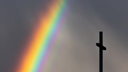 Köln: Ein kräftiger Regenbogen ist am dunklen Himmel neben dem Kreuz einer Kirche zu sehen.