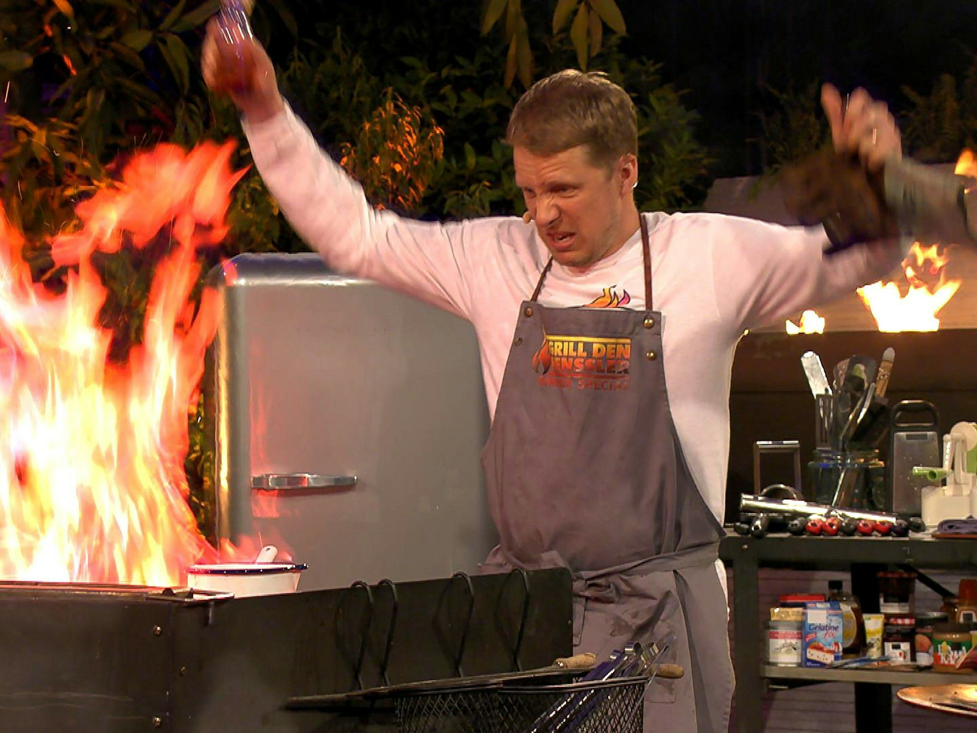 Oliver Pocher steht bei „Grill den Henssler“ vor einer lodernden Flamme in der Küche.
