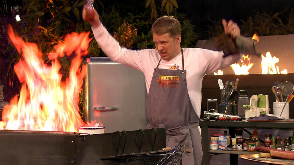 Oliver Pocher steht bei „Grill den Henssler“ vor einer lodernden Flamme in der Küche.