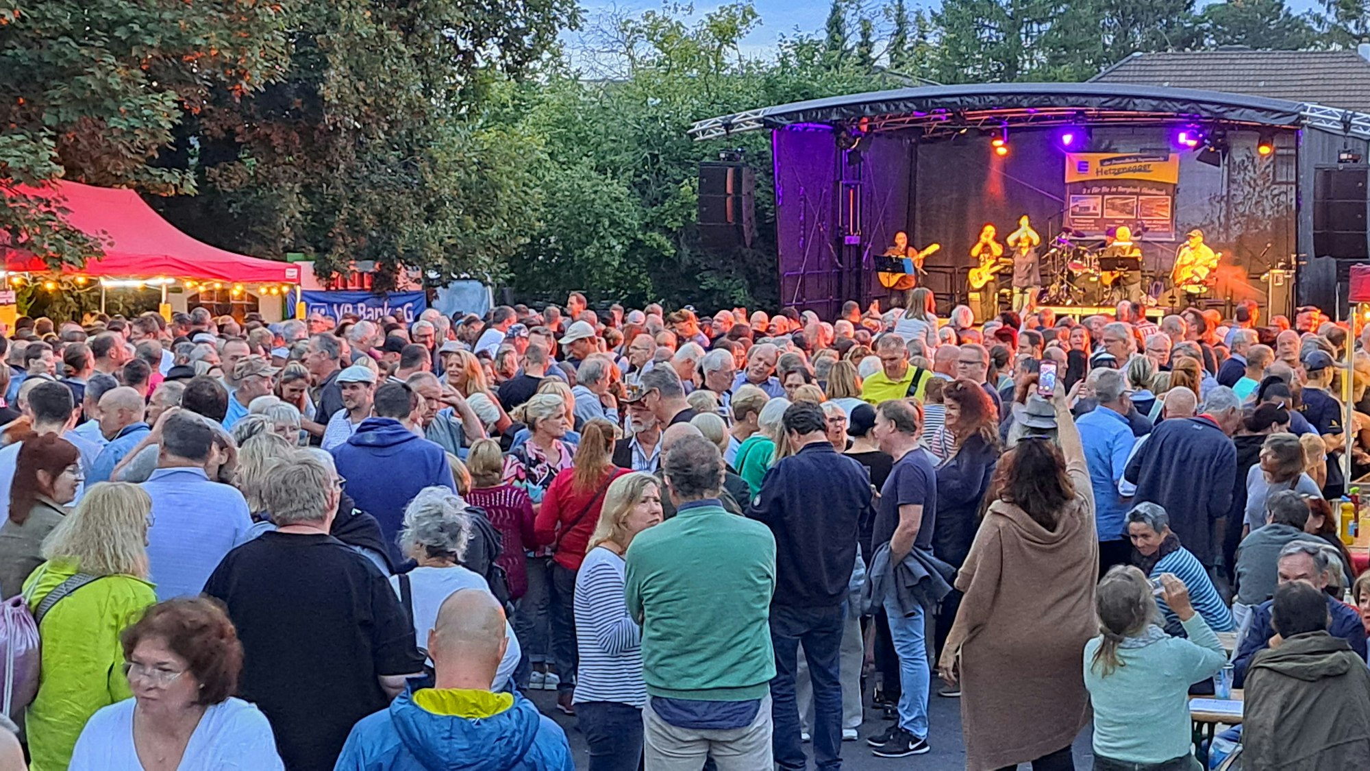 Der Dorfplatz in Bergisch Gladbach-Sand ist voll von Menschen, im Hintergrund steht eine Bühne von der die Band Clearwater spielt.