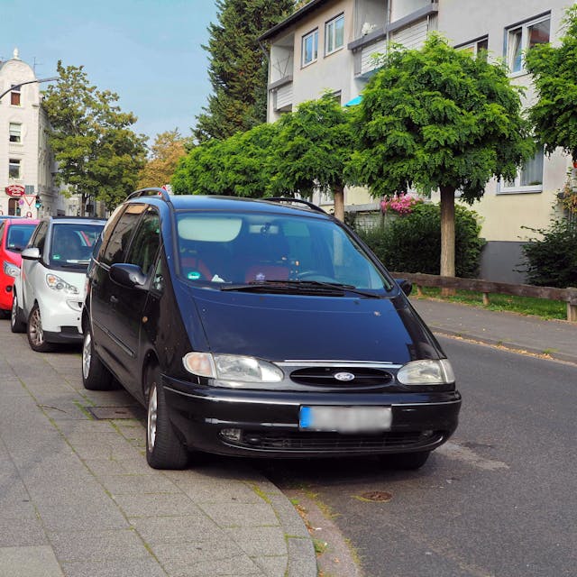 Mehrere Autos parken hintereinander an einer Straße, sie stehen halb auf dem Bürgersteig.