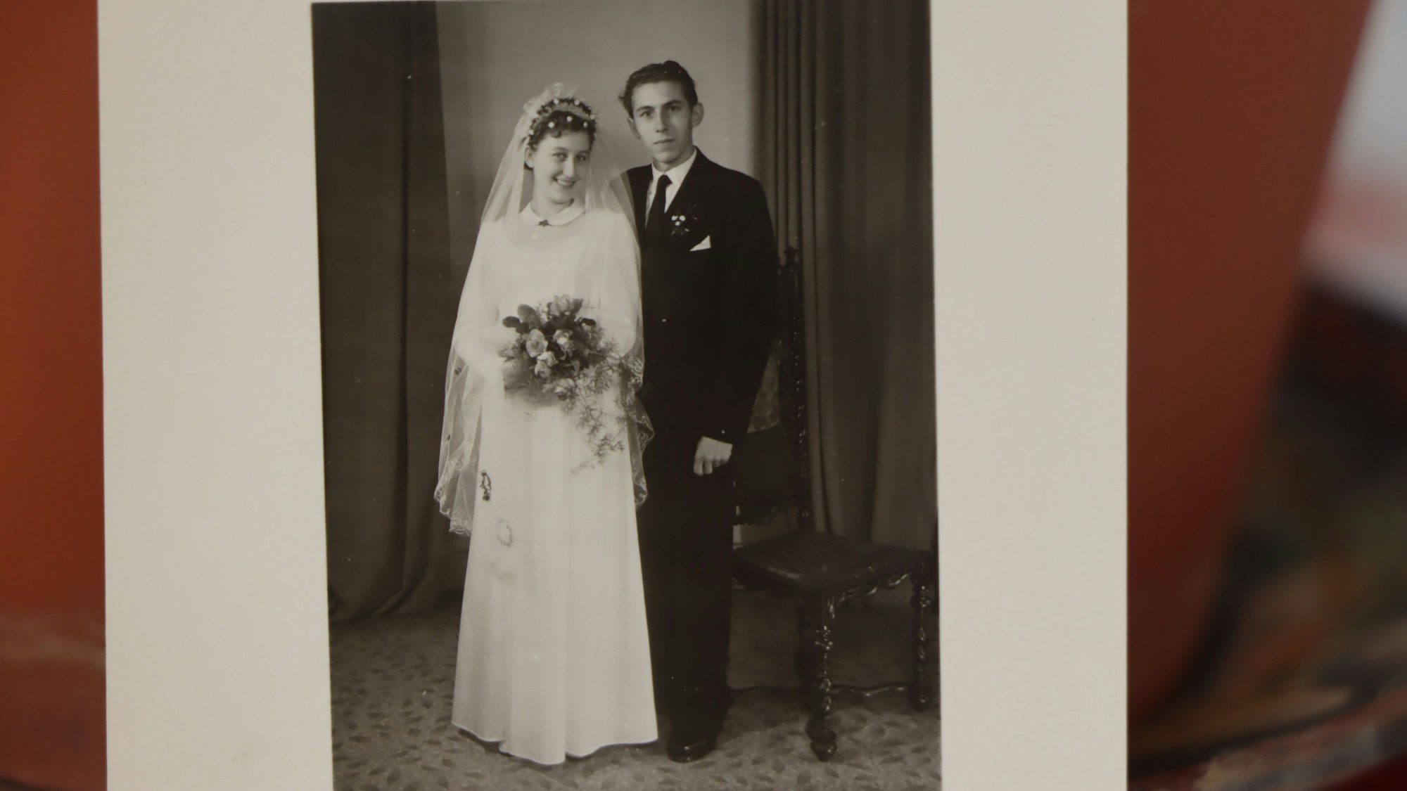Eine alte Schwarzweiß-Fotografie zeigt ein junges Ehepaar, sie im weißen Kleid, er im dunklen Anzug.
