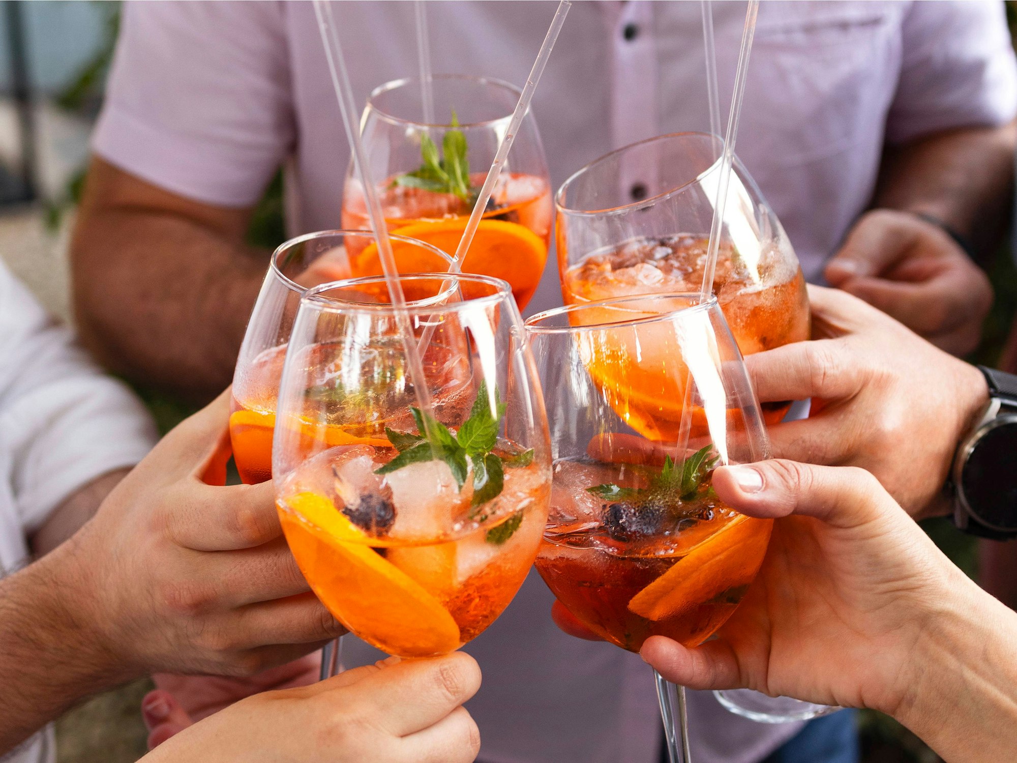 Vier Personen stoßen mit Gläsern, die mit dem orangen Aperol Spritz gefüllt sind, an.