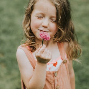 Ein kleines Mädchen hält eine Kornblume vor den Mund und hat die Augen geschlossen, als Geste der Dankbarkeit.