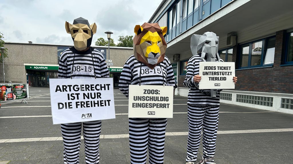Drei wie Häftlinge verkleidete Aktivistinnen und Aktivisten, mit Demo-Bannern und Tierkopf-Masken.