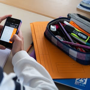 Ein Mädchen hält ein Smartphone im Klassenraum ein Smartphone in der Hand.&nbsp;