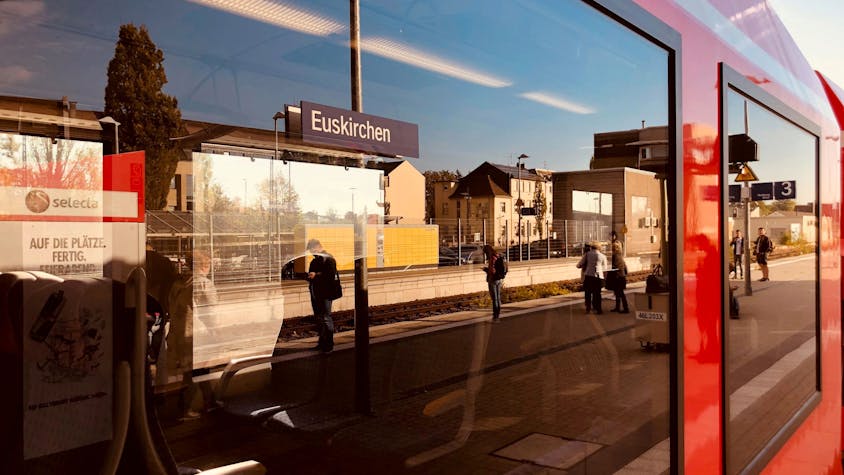 In der Fensterscheibe eines Regionalzuges spiegelt sich ein Bahnsteig mit wartenden Reisenden im Bahnhof Euskirchen.