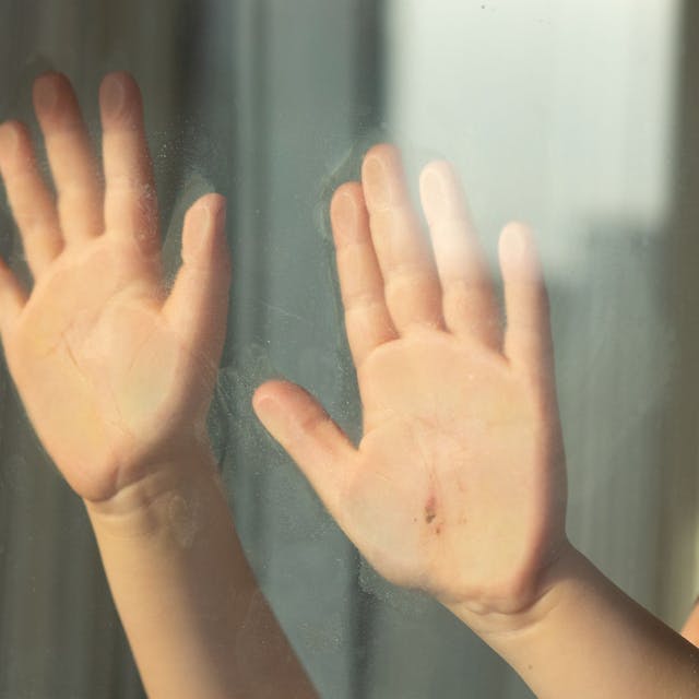 Kinderhände halten sich an einer Glasscheibe fest.