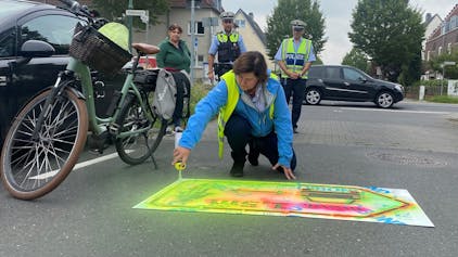 Christiane Jäger, Fachbereichsleiterin für Mobilität und Klimaschutz, sprayt einen signalfarbenen Hinweis auf die Straße.