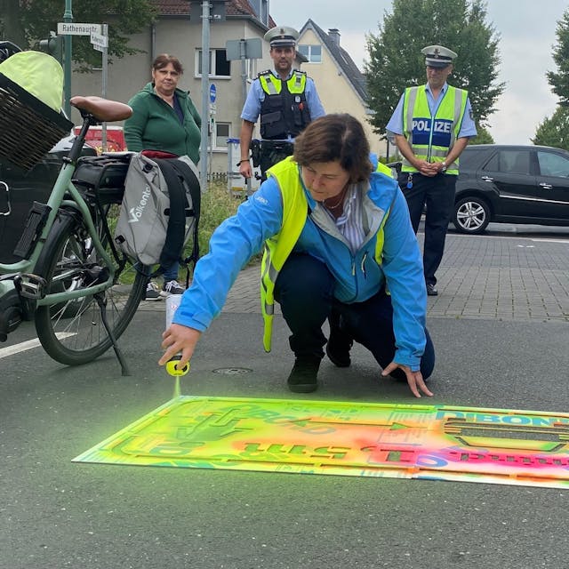 Christiane Jäger, Fachbereichsleiterin für Mobilität und Klimaschutz, sprayt einen signalfarbenen Hinweis auf die Straße.