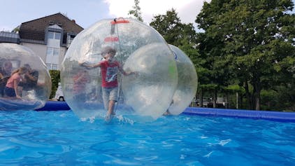 Ein Kind spielt in einer großen Kugel auf dem Wasser.