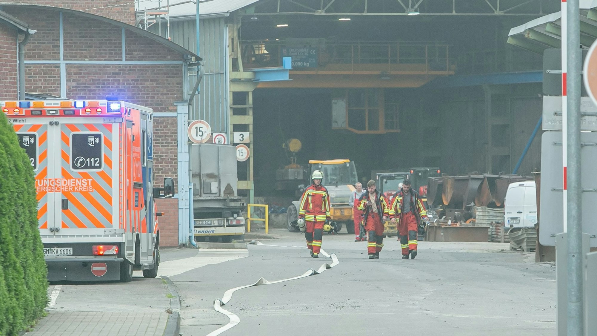 Feuerwehrleute vor einer Werkshalle, links steht ein Fahrzeug des Rettungsdienstes.