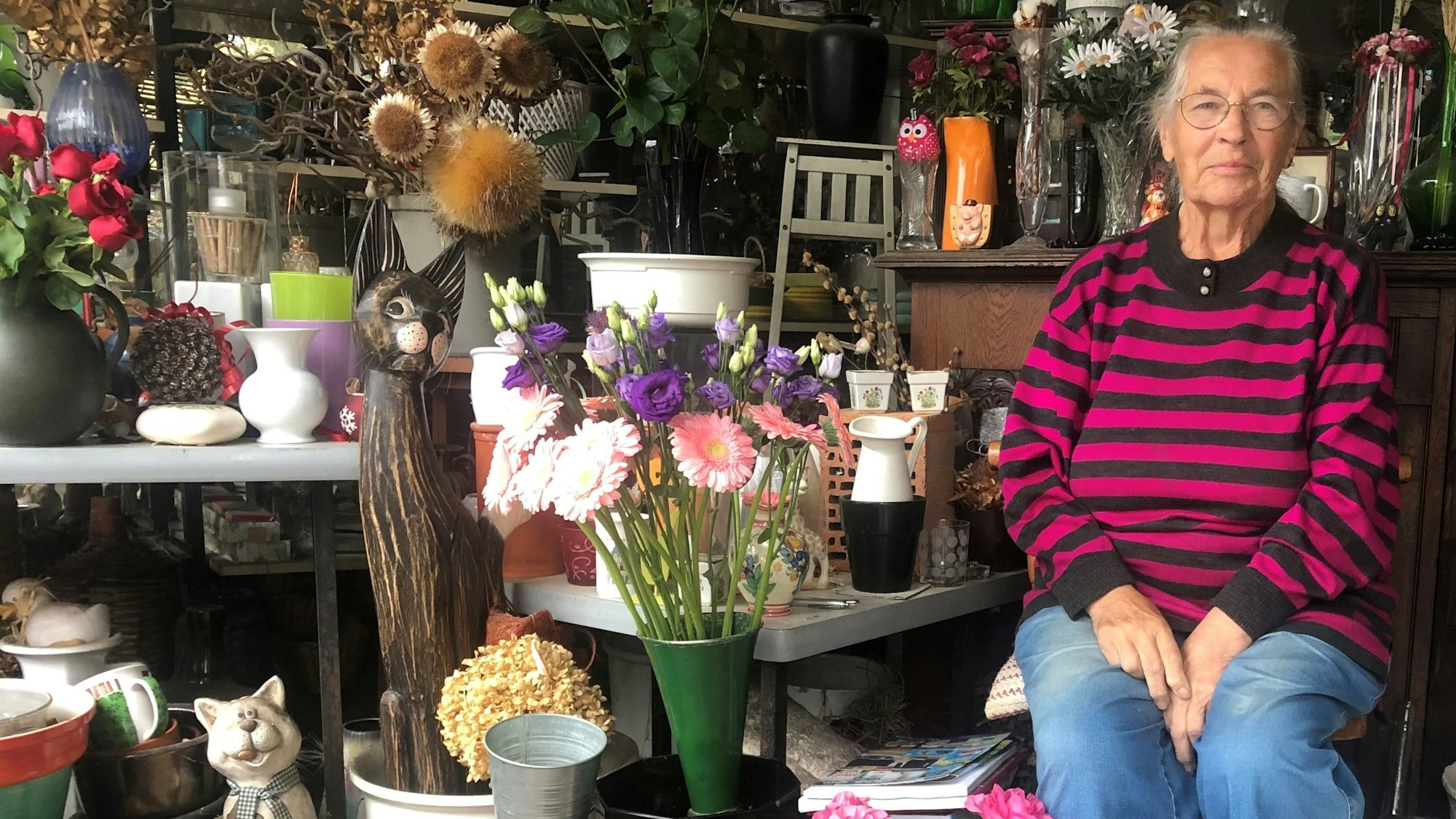 Eine alte Frau im Ringelpulli sitzt in einem Blumenladen