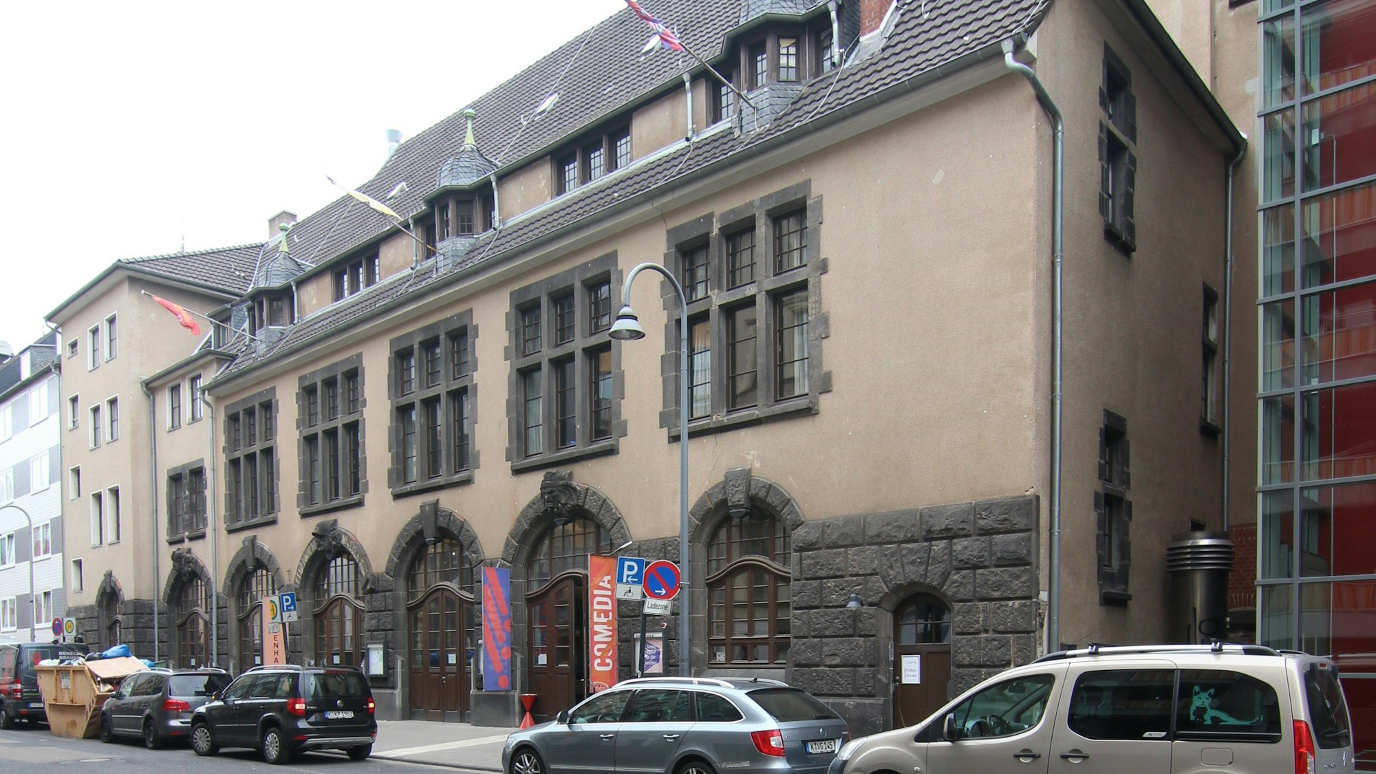 Auf dem Bild zu sehen ist die ehemalige Feuerwache, die heute das Comedia-Theater beherbergt. Unten am Gebäude und an den Fenstern sieht man noch eine alte, graue Steinfassade, der Rest der Wand ist bräunlich.