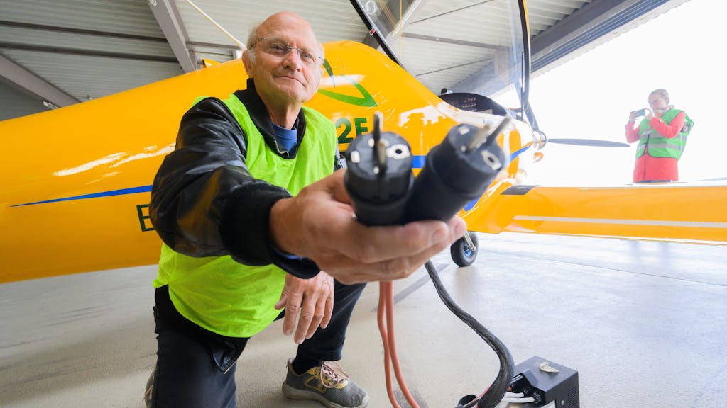 Testpilot Uwe Nortmann zeigt einen Spannungswandler vor dem E-Flugzeug „Elektra Trainer“ am Flughafen Hannover, hier im August 2023.