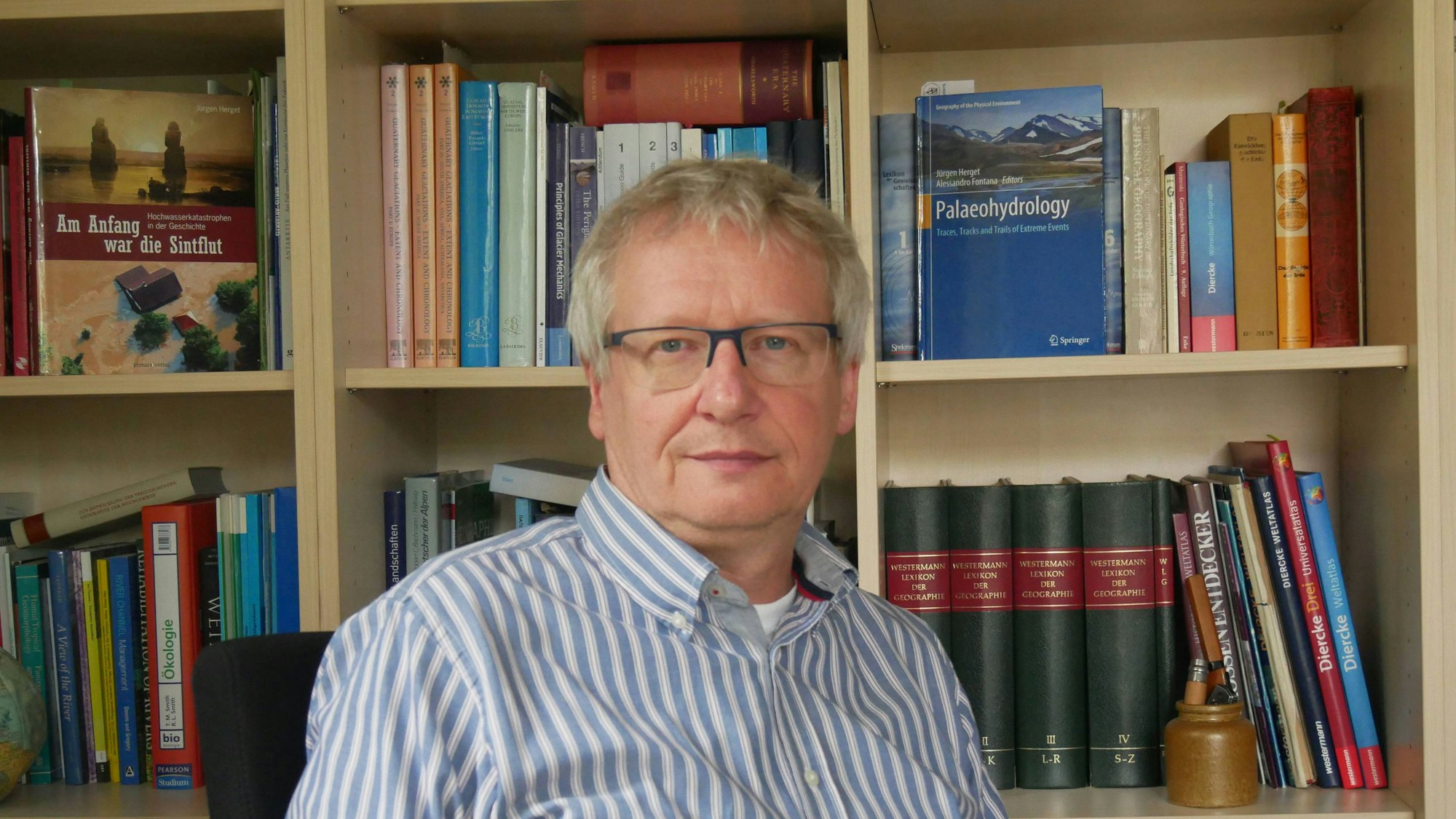 Professor Dr. Jürgen Herget. Im Hintergrund eine Bücherwand mit Fachliteratur.