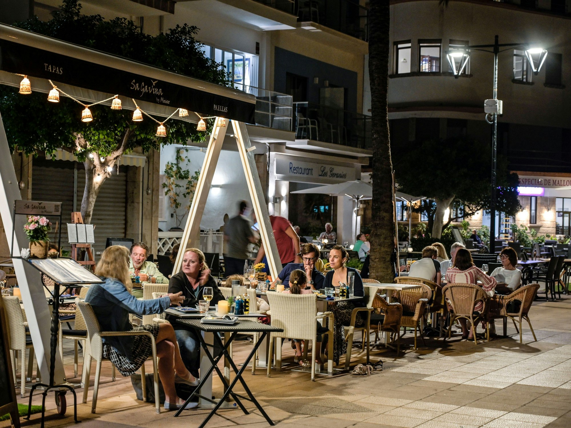 Menschen sitzen in Restaurants an der Strandpromenade von Port de Soller auf Mallorca.