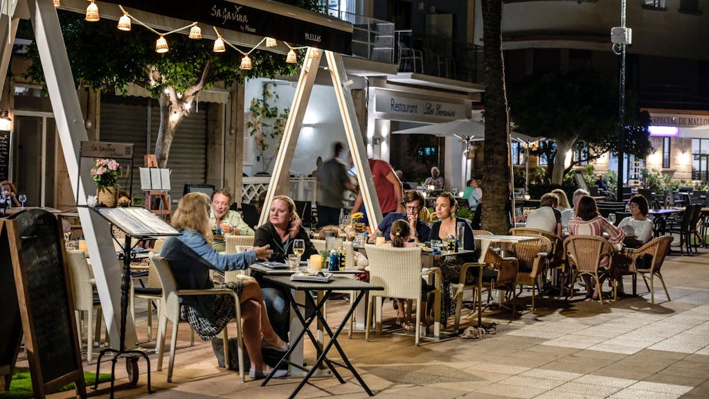 Menschen sitzen in Restaurants an der Strandpromenade von Port de Soller auf Mallorca.
