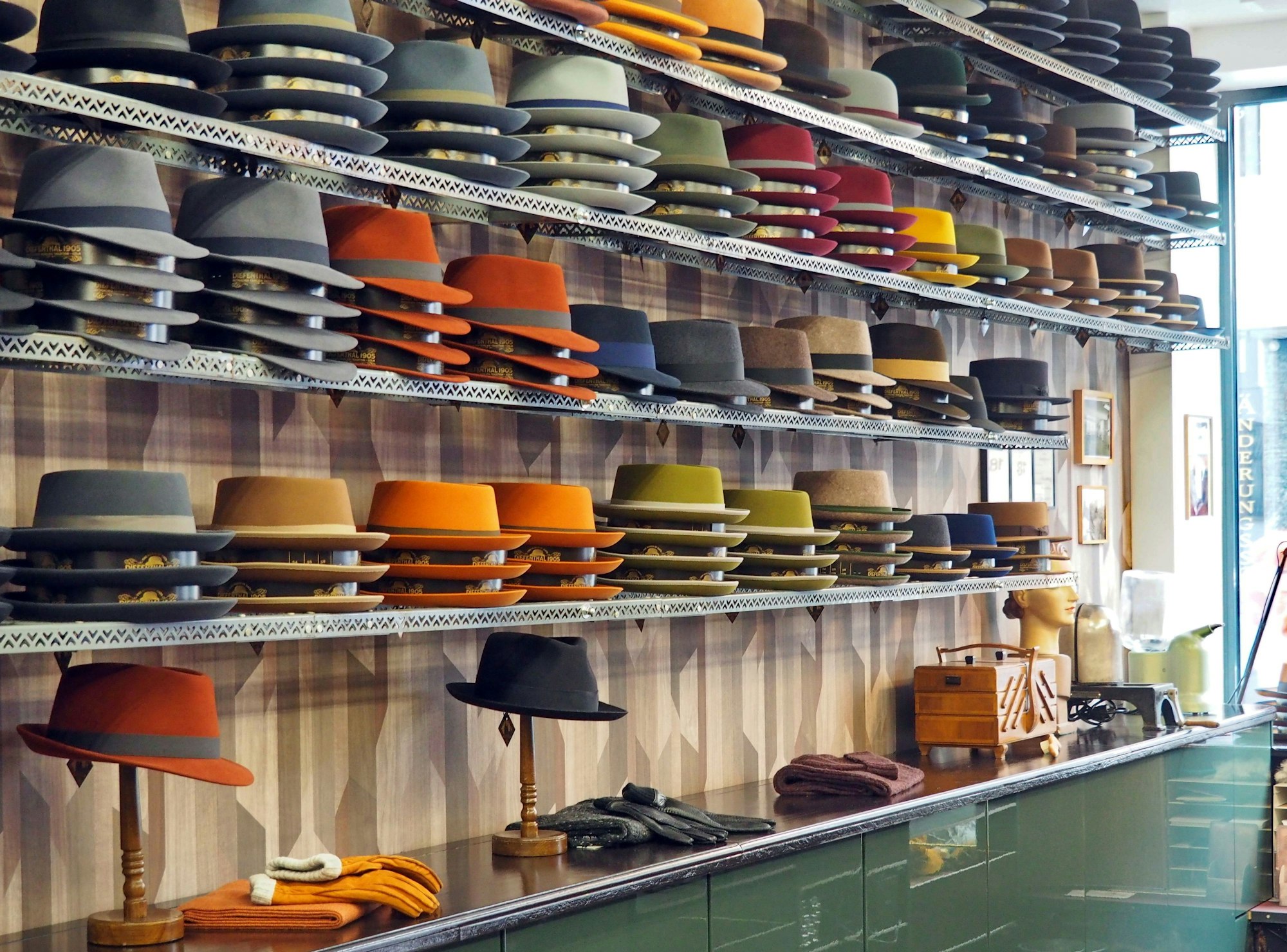 Hüte in verschiedenen Formen und Farben liegen auf langen Regalen.