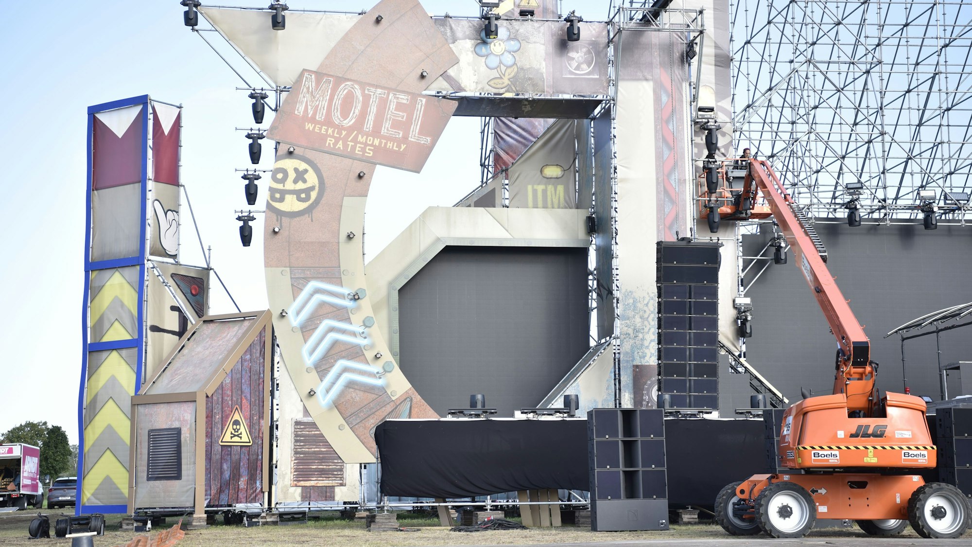 Das Bild zeigt den linken Teil einer großen Festivalbühne. Rechts arbeiten zwei Mitarbeiter auf einem Hubsteiger am Bühnenbild.