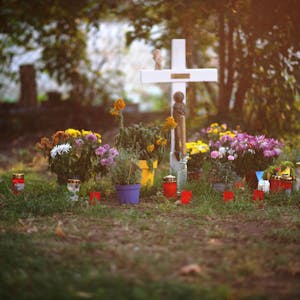 Das Bild zeigt ein weißes Holzkreuz, Blumen und Kerzen. Sie erinnern an den Tod eines Wohnungslosen.
