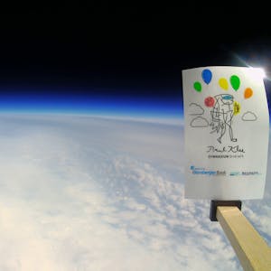 Die gekrümmte Erdoberfläche ist unter einer Wolkendecke vor dem dunklen Hintergrund des Weltalls zu sehen. Rechts ragt eine Karte mit der Aufschrift Paul-Klee-Gymnasium ins Bild.