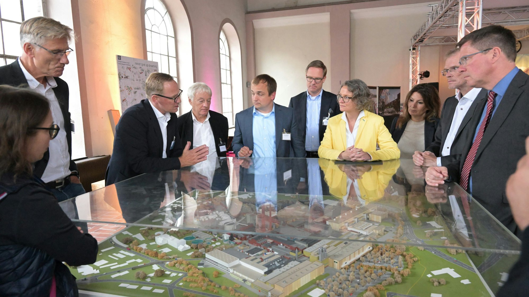 Ministerin Ina Scharrenbach steht mit zwei Frauen und vielen Männern um ein Modell des Zanders-Geländes.