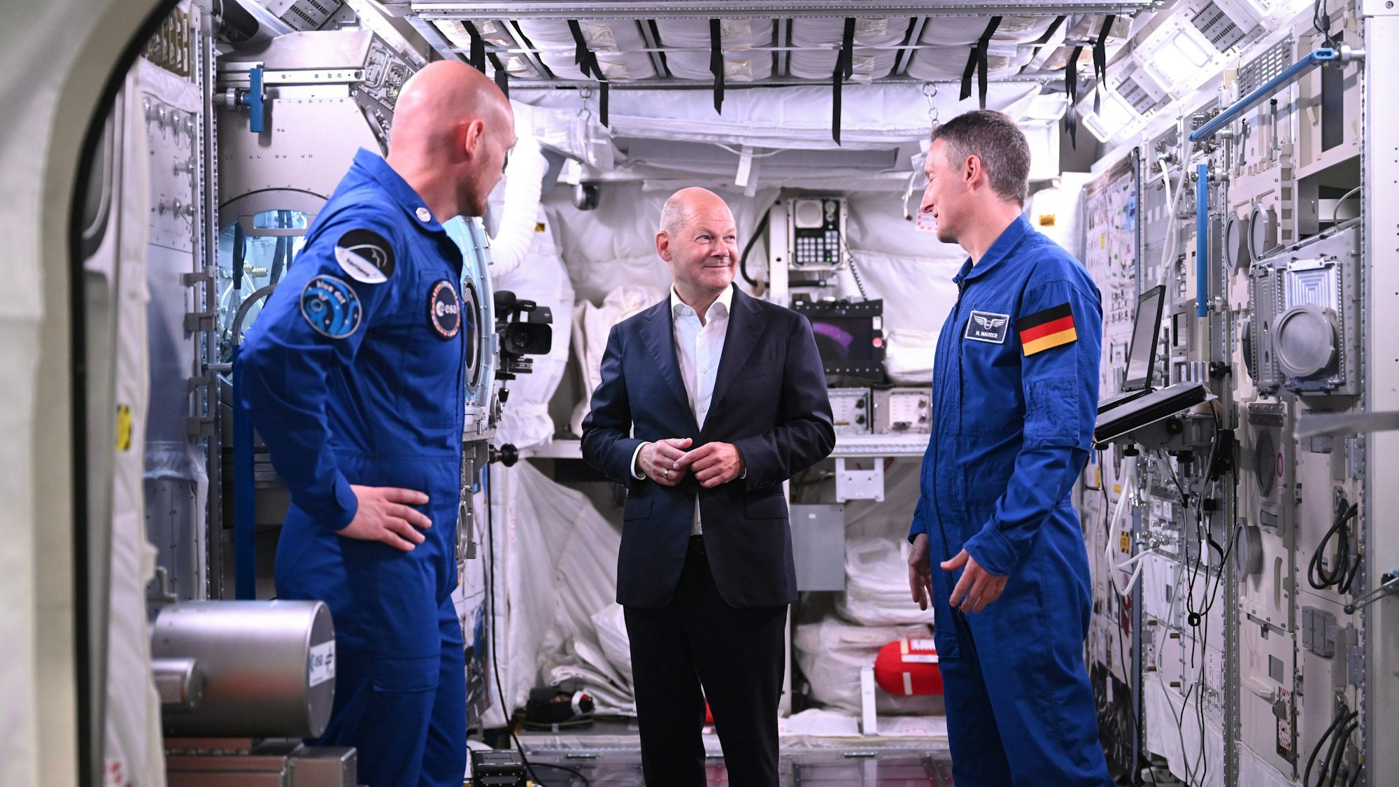 Bundeskanzler Olaf Scholz (SPD, M) im Gespräch mit den deutschen ESA-Astronauten Matthias Maurer (r) und Alexander Gerst in einem Modell des Columbus-Moduls in der Neutral Bouyancy Facility