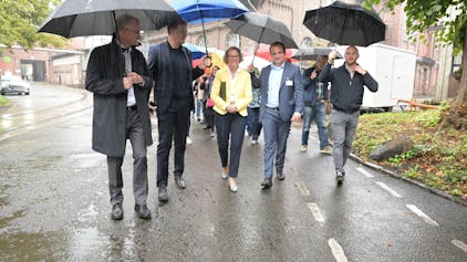 NRW-Bauministerin Ina Scharrenbach (CDU) geht mit lokalen Verantwortlichen unter Regenschirmen übers Zandersgelände.