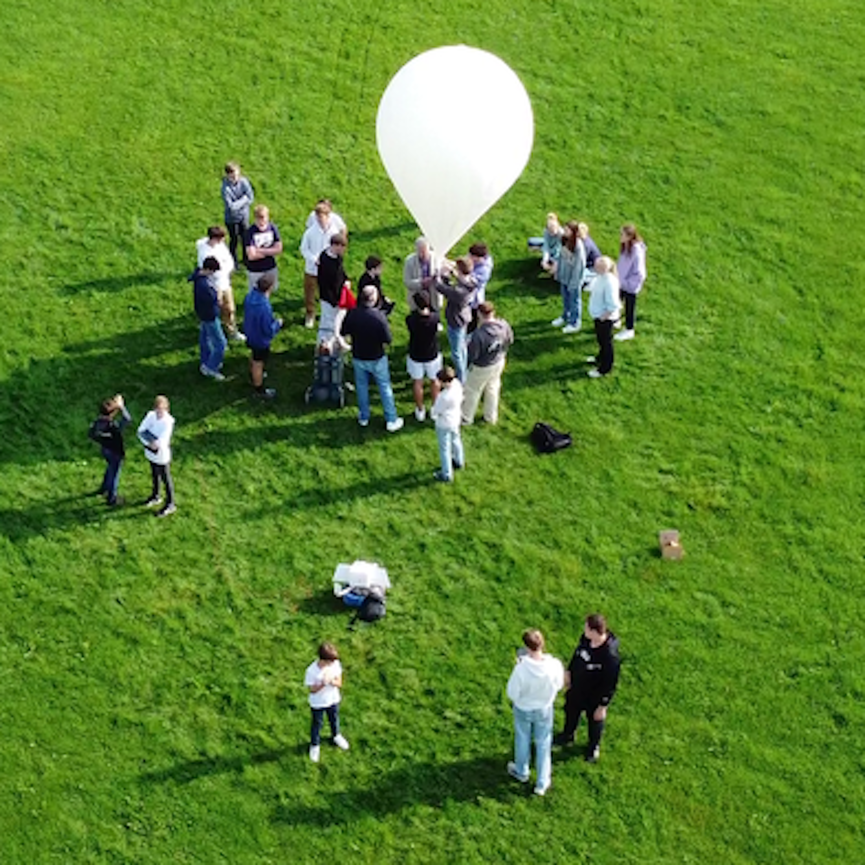 Eine Gruppe von Schülern steht auf einer Wiese, über ihnen schwebt ein weißer Ballon.