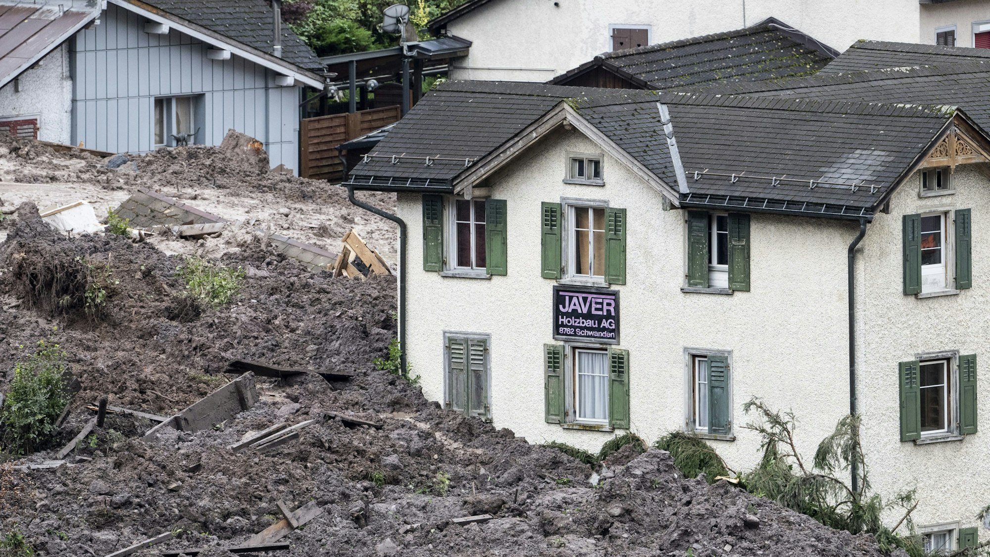 Geröll und Schlammmassen umgeben Häuser nach einem Erdrutsch.