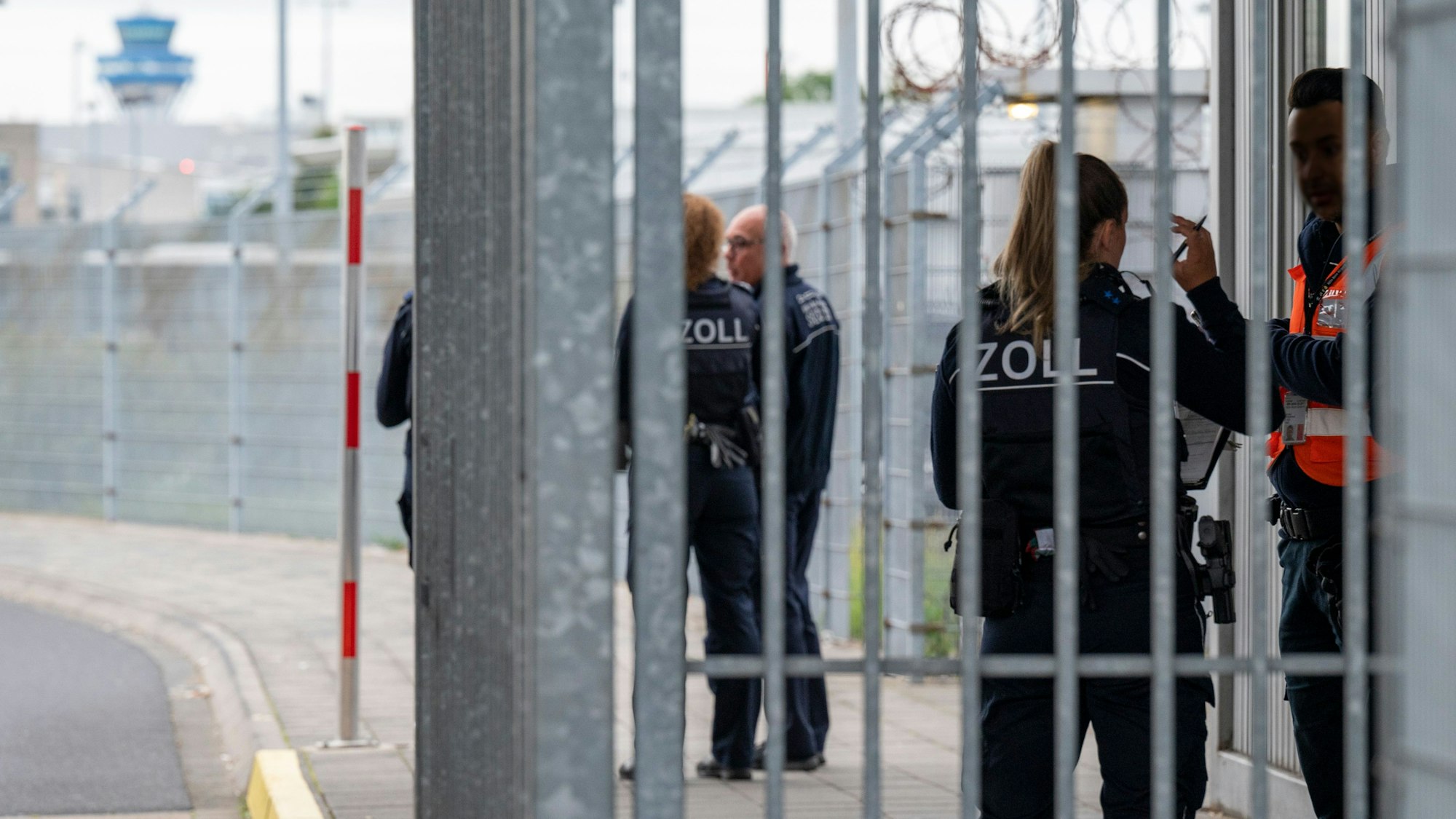 Beamten und Beamtinnen des Zolls stehen am Lieferanteneingang des Flughafens Köln-Bonn und kontrollieren einen Sicherheitsmann
