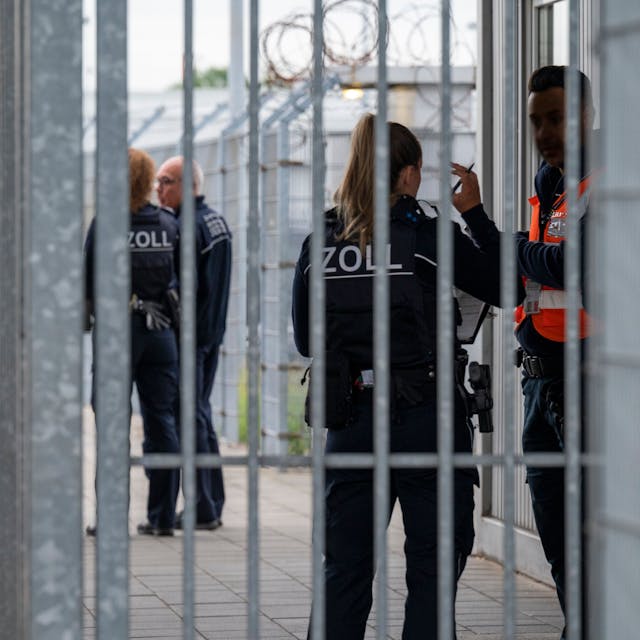 Beamten und Beamtinnen des Zolls stehen am Lieferanteneingang des Flughafens Köln-Bonn und kontrollieren einen Sicherheitsmann