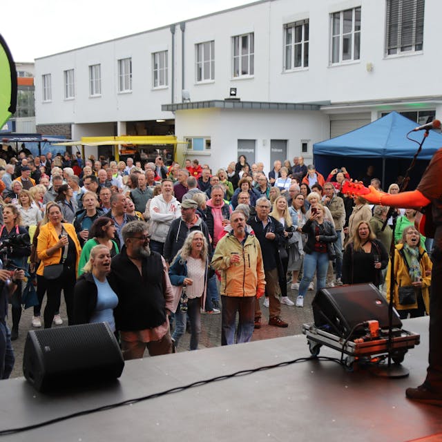 Der Sänger Björn Heuser steht mit Gitarre auf einer Bühne, vor der die Zuschauer begeistert mitsingen.