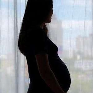 Eine schwangere Frau steht im Gegenlicht. Es ist nur die Silhouette zu sehen.