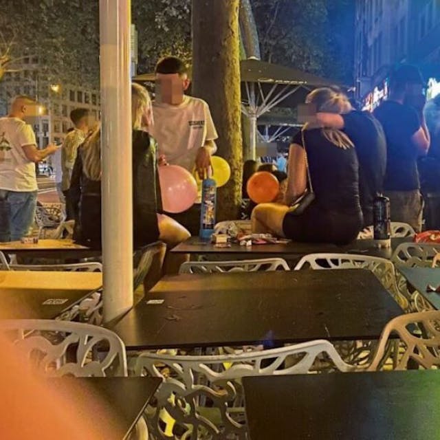 Junge Männer und Frauen sitzen mit Luftballons voller Lachgas auf Tischen an den Kölner Ringen.