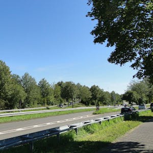 Eine mehrspurige Straße mit Bäumen links und rechts ist zu sehen.