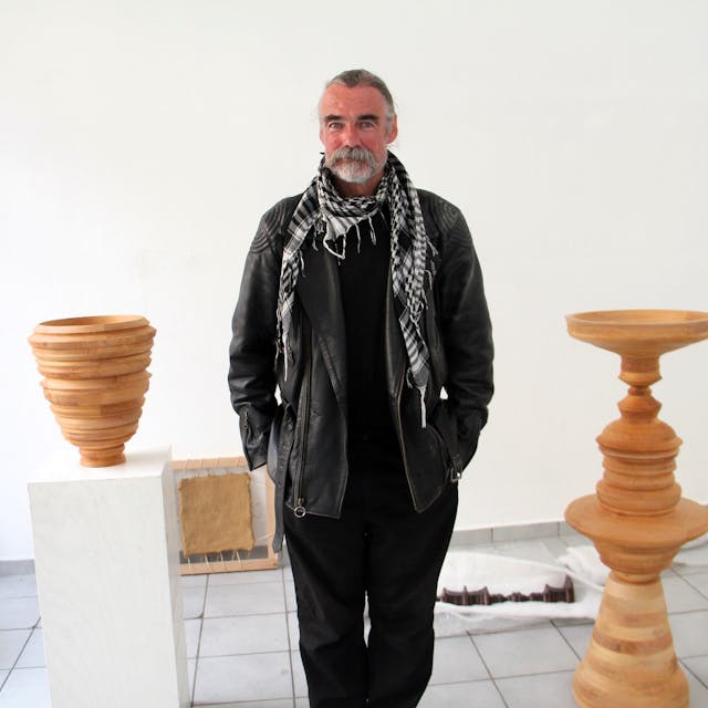 Ein Mann mit grauem Bart stehen zwischen Skulpturen in einem Raum.
