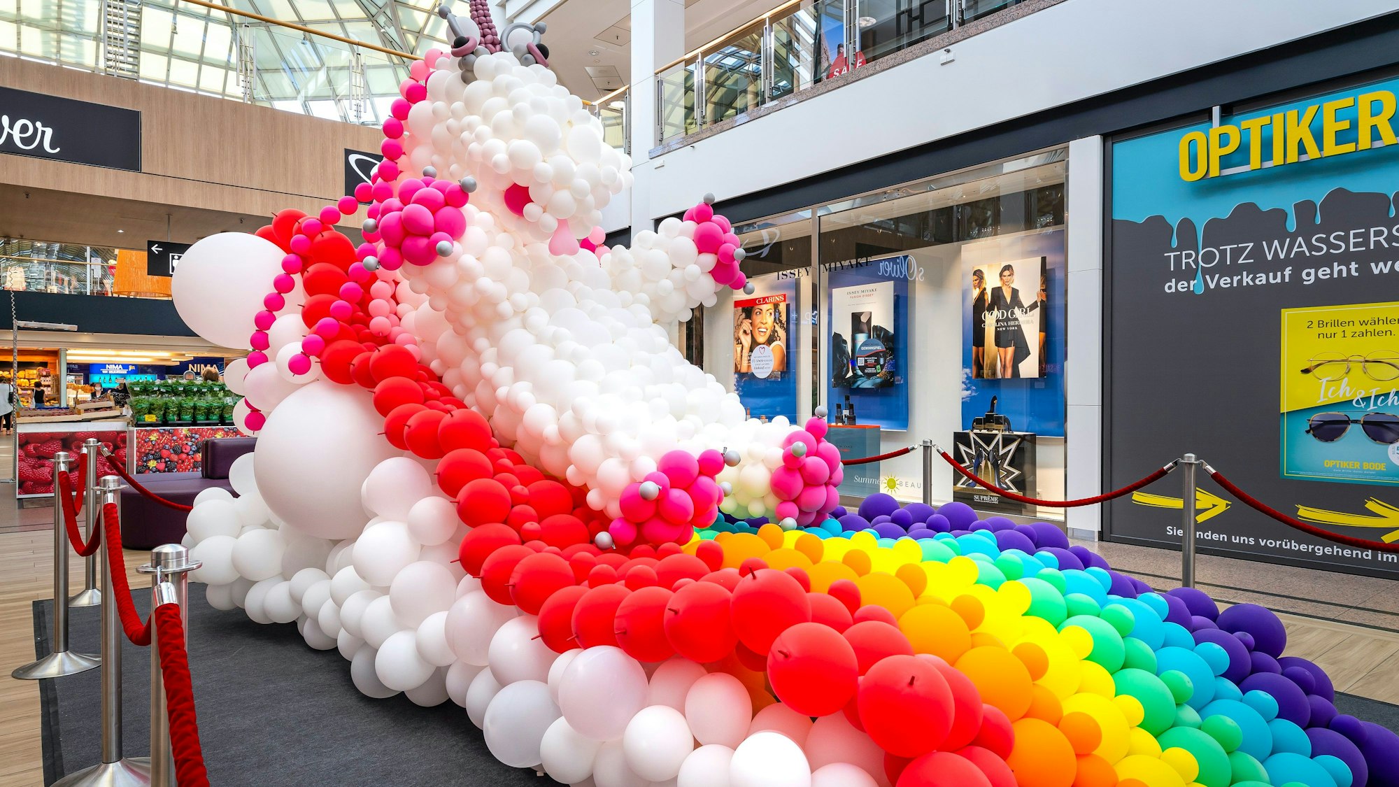 Ein Einhorn mit Regenbogen aus Luftballons steht im Erdgeschoss eiens großen Einkaufszentrums.